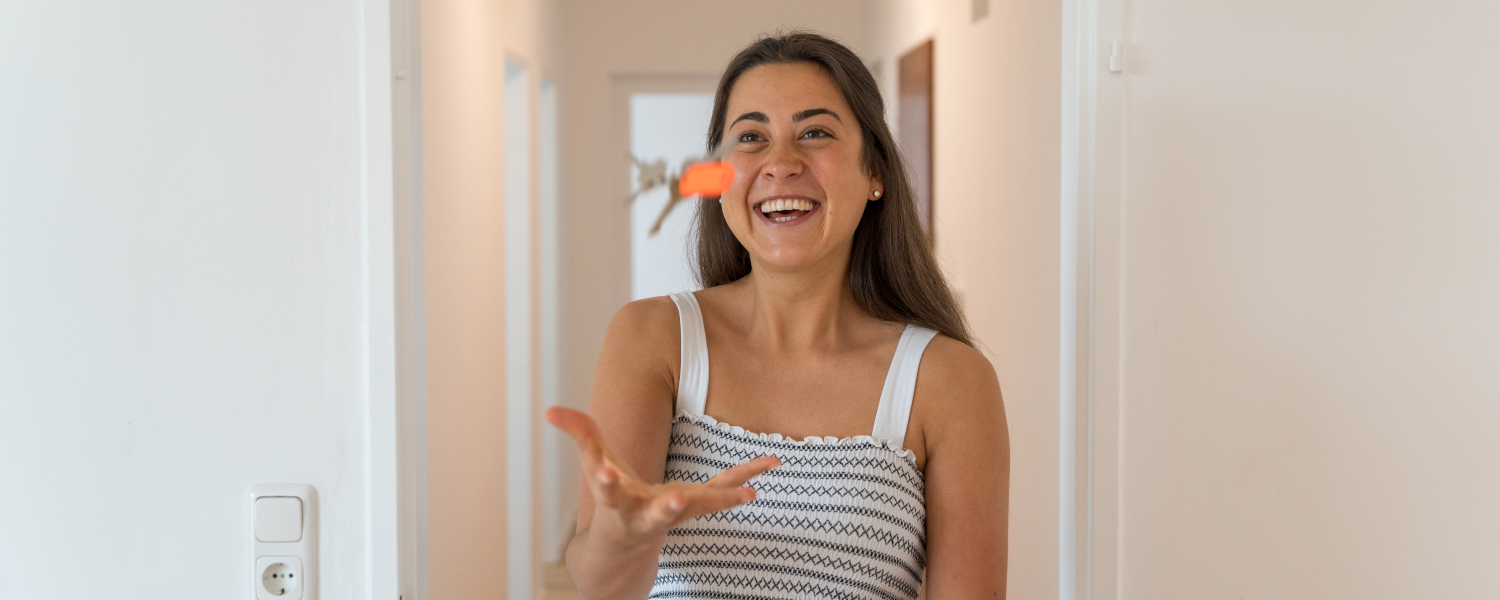 Eine junge Frau lacht und wirft ihren Wohnungsschlüssel in die Luft