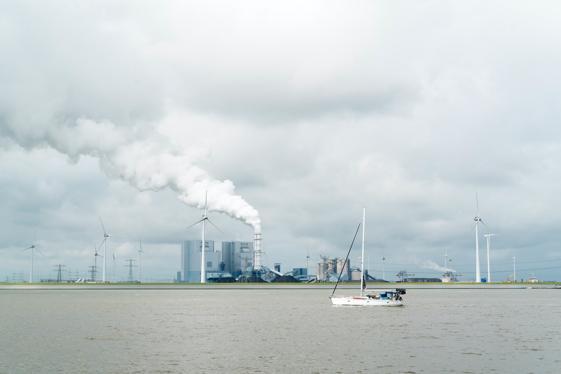 weißes Segelboot mit Fabrik-Emissionen im Hintergrund