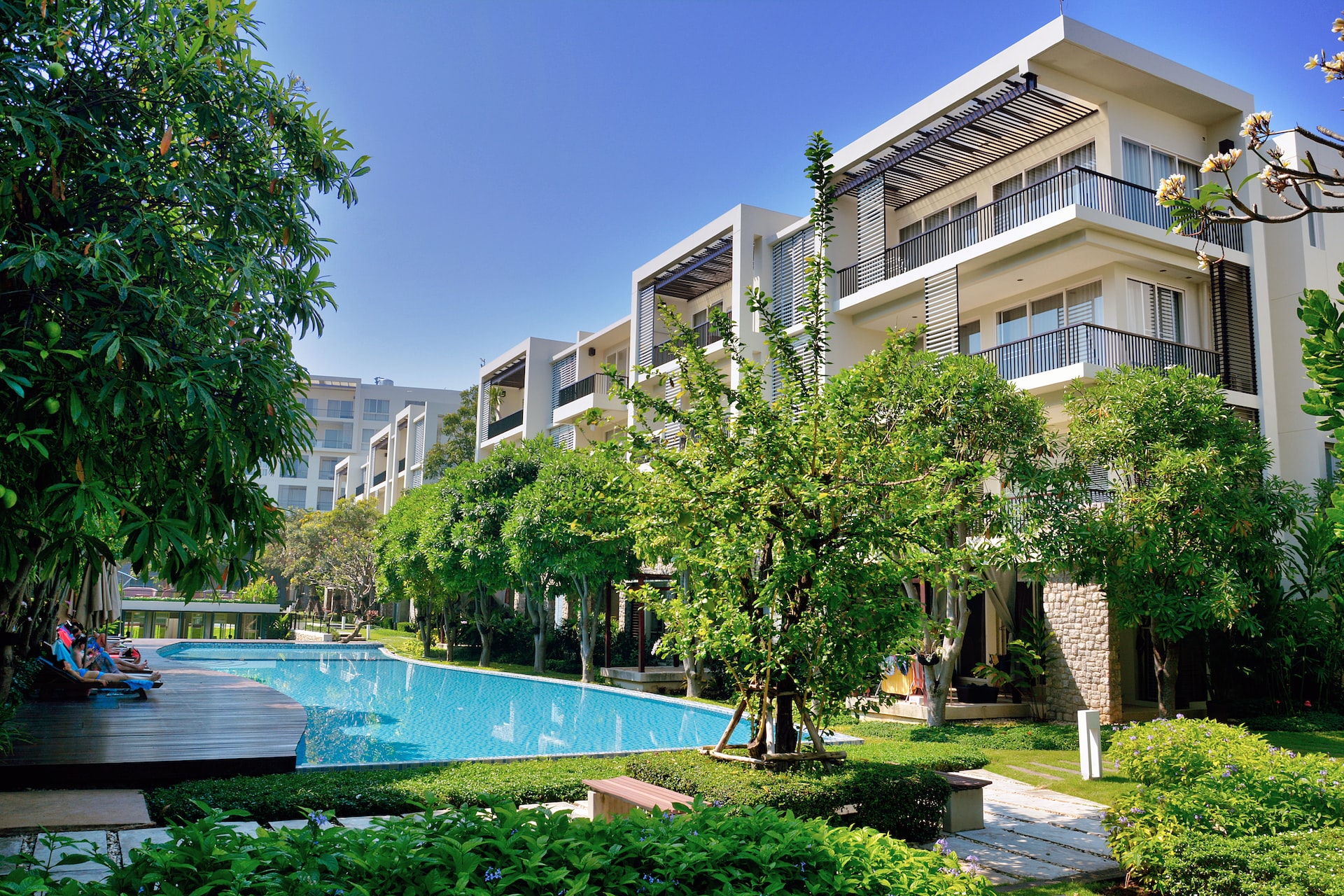 Luxuriöser Apartmentkomplex vor blauem Himmel, mit grünen Bäumen und einem riesigen Pool